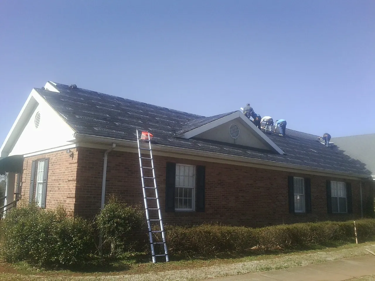 Crew tearing shingles off a brick ranch roof with a ladder set — Emergency Roof Repair work by our crew in New Rochelle