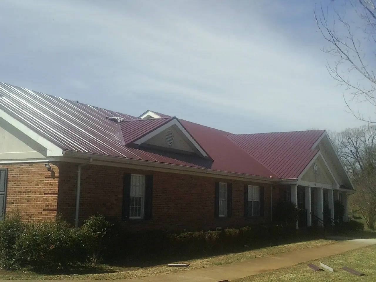 Red metal roof with gabled entries on a long brick building, from a Hail Damage Roof Repair job in New Rochelle
