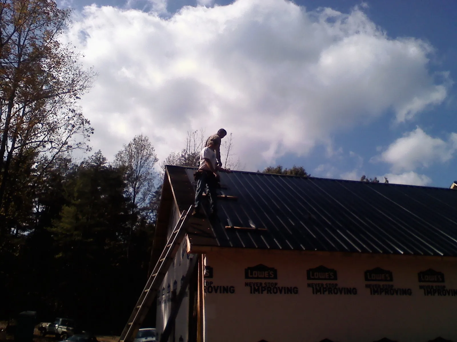Roofer fastening dark metal panels high against a cloudy sky, from a Roof Inspection job in New Rochelle
