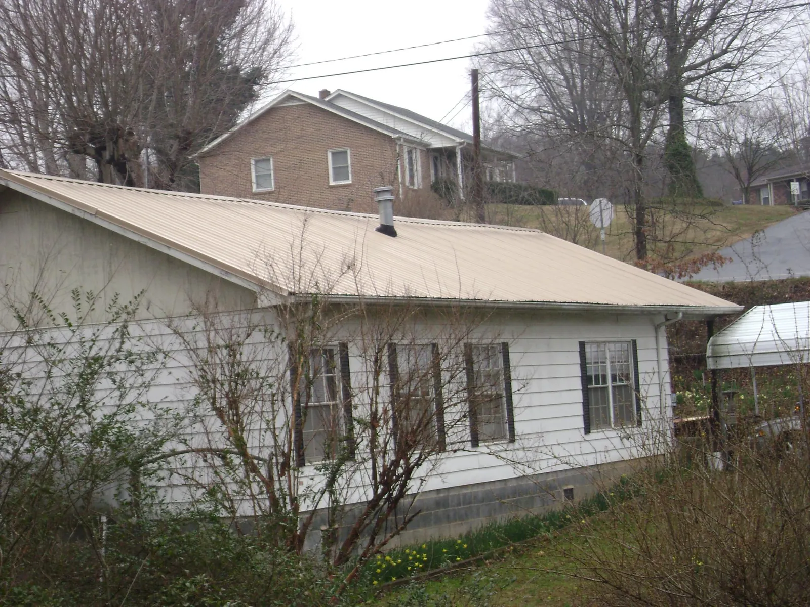 Tan metal roof on a white sided house set into a hillside — Commercial Roofing by Roofing Brothers in New Rochelle